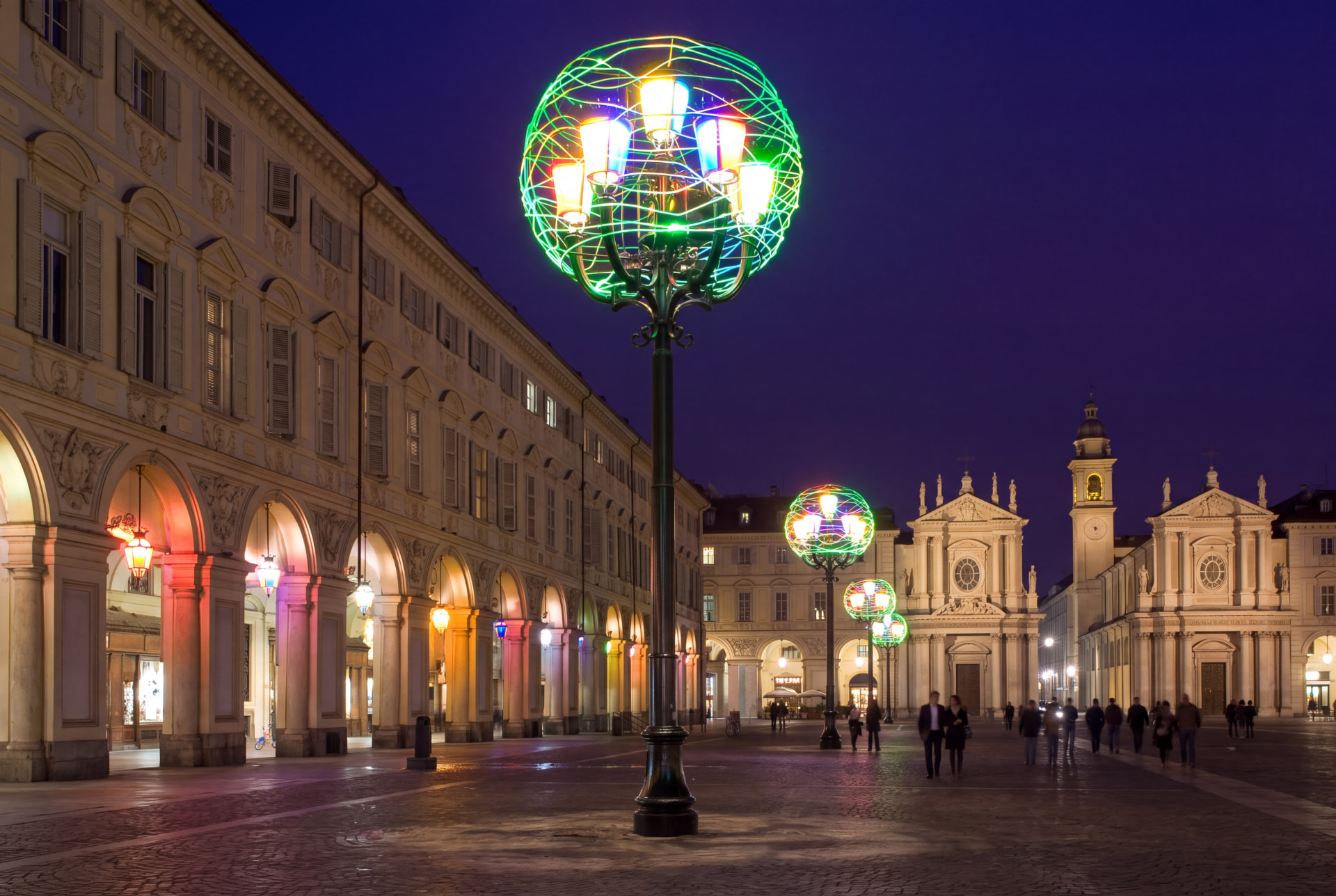 Piazza San Carlo in Turin at night, lit by colourful spherical holiday lights, with the twin churches in the background