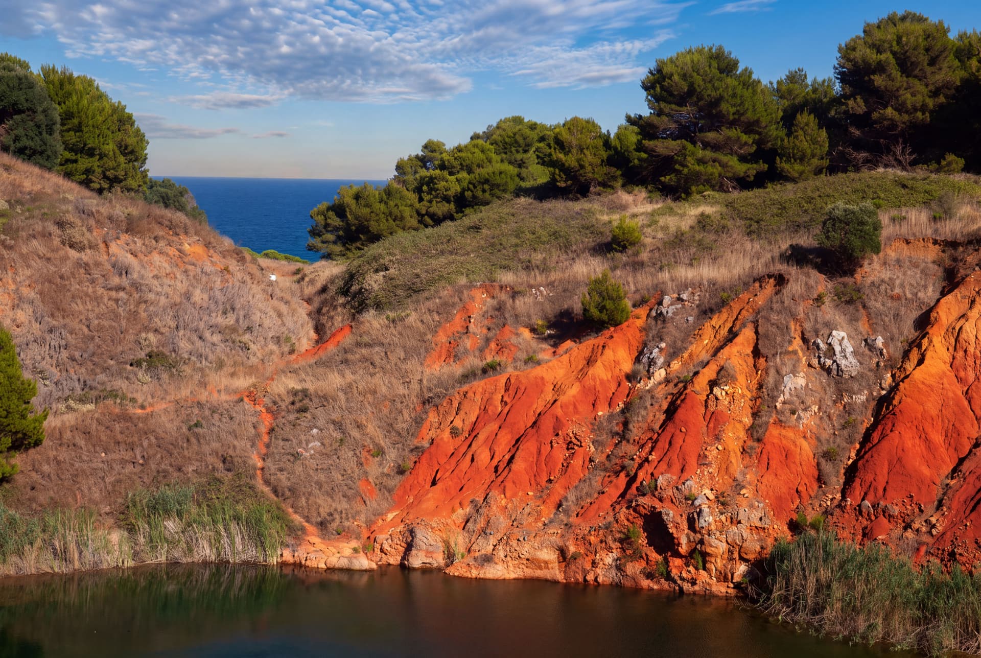 Red bauxite cliffs above a small lake with pine trees and the sea in the background