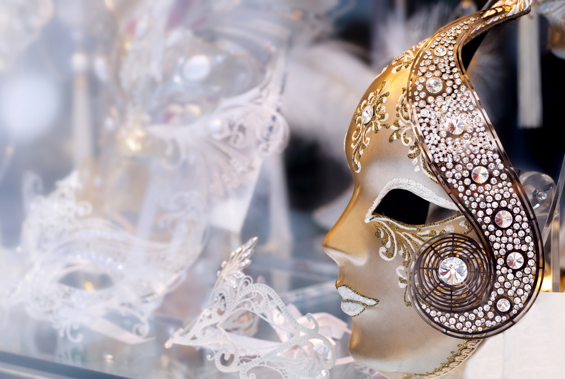 Golden carnival mask decorated with crystals, with white lace masks blurred in the background
