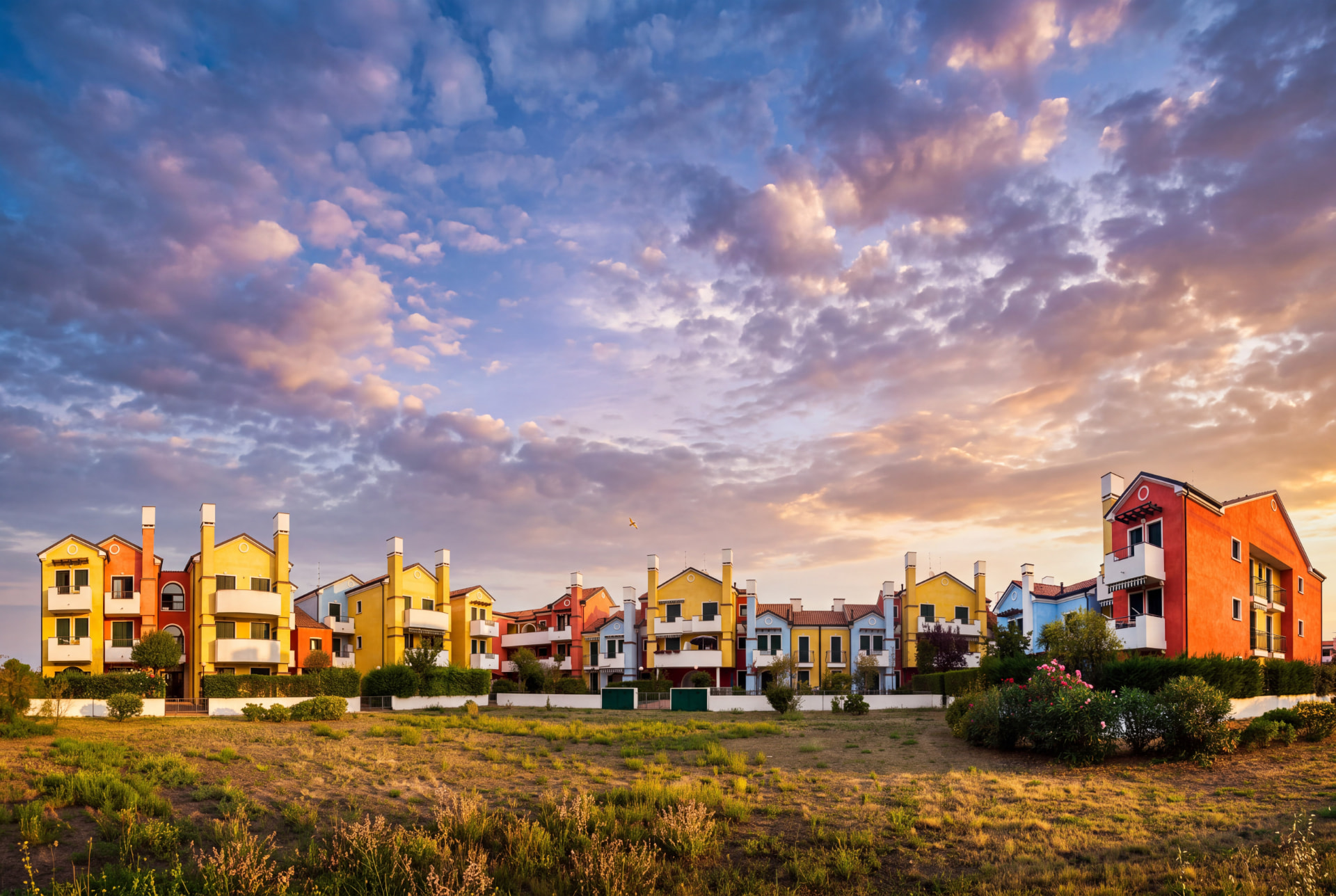 Row of colourful yellow, orange and blue houses under a dramatic pink and purple sunset sky