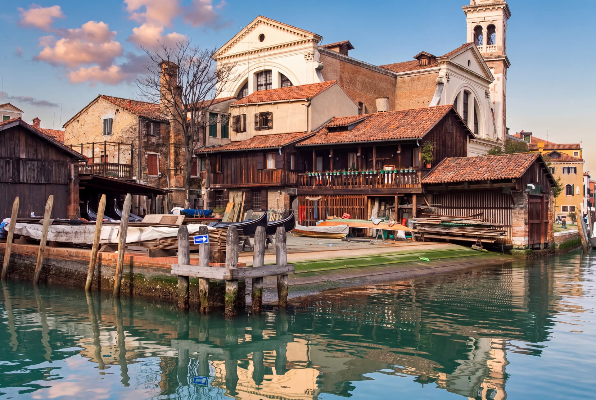 Traditional Venetian gondola workshop beside a canal, with gondolas, wooden sheds and the church of San Trovaso behind it
