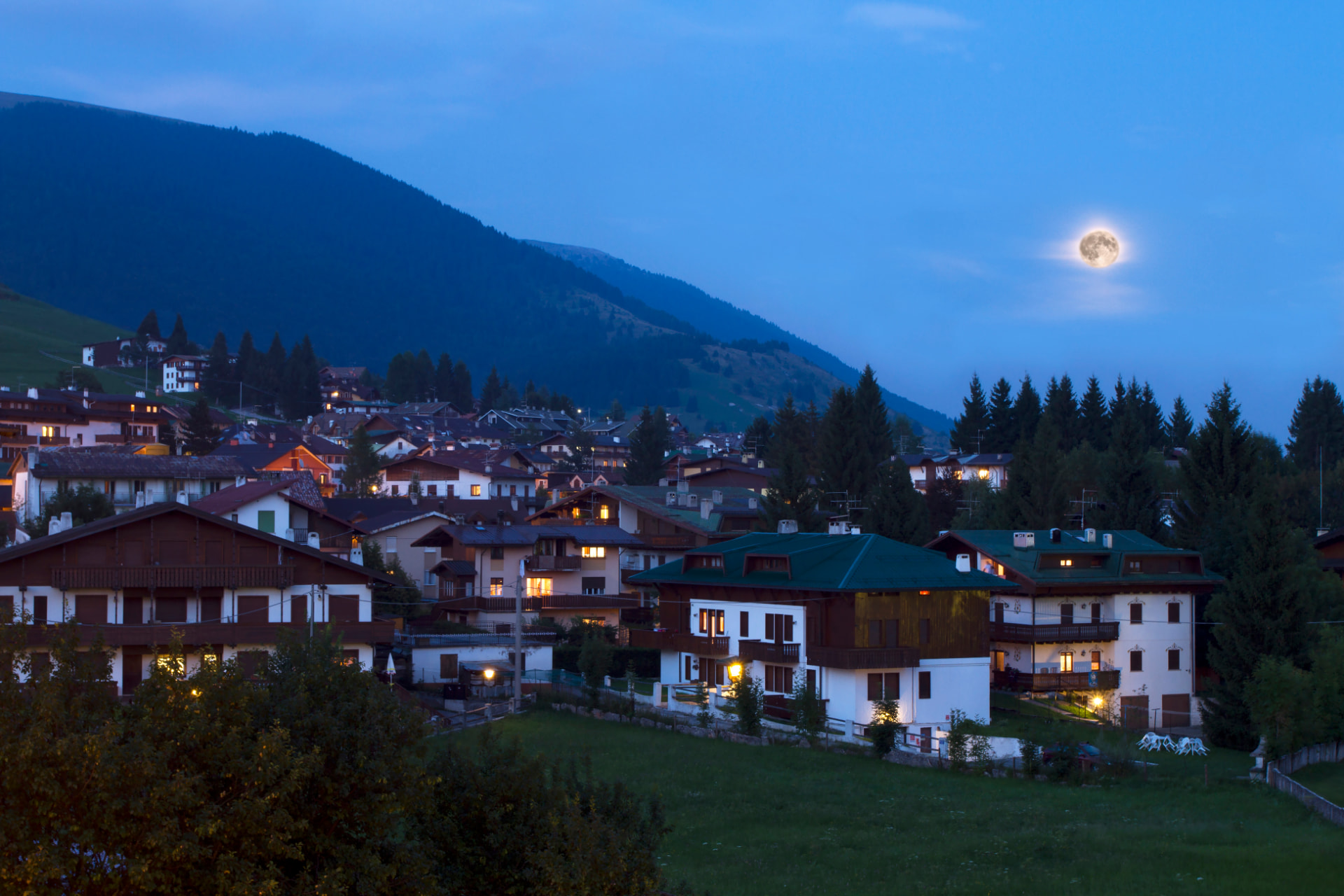 Mountain village lit at dusk under a moon