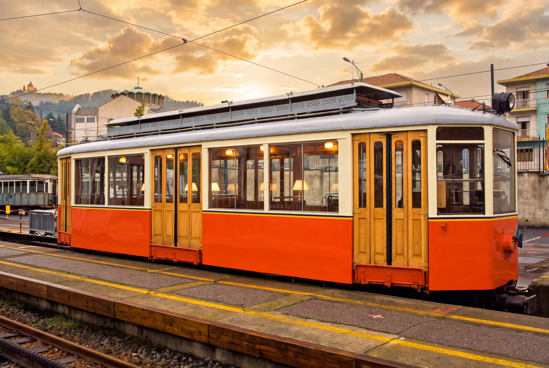 Vintage orange and cream tram at a stop under a golden cloudy sunset sky