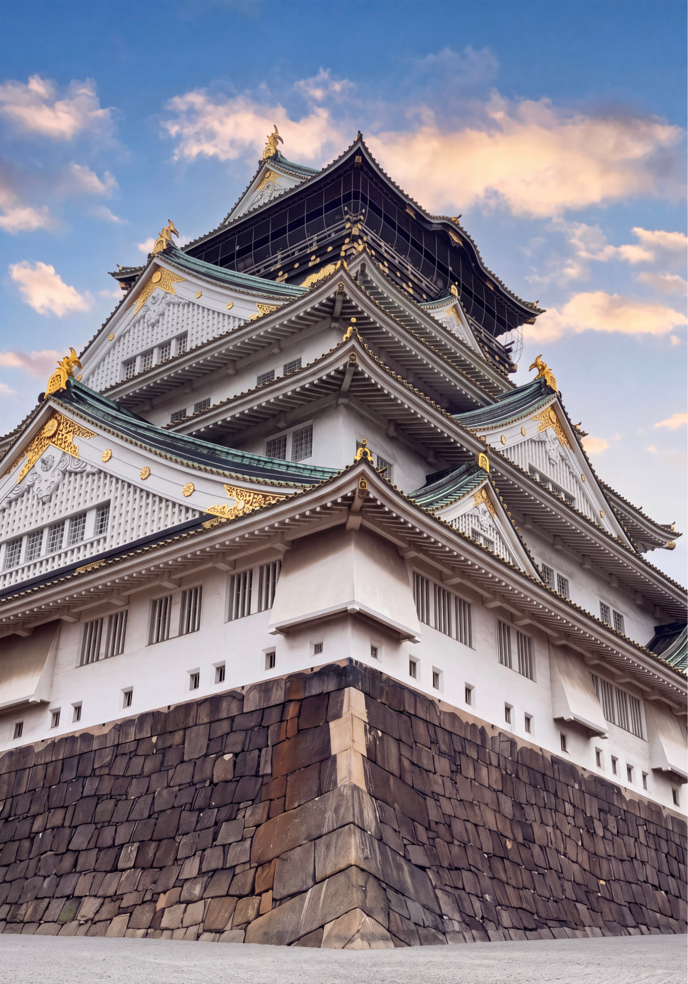 Osaka Castle seen from below with white walls and green roofs against a sunset sky