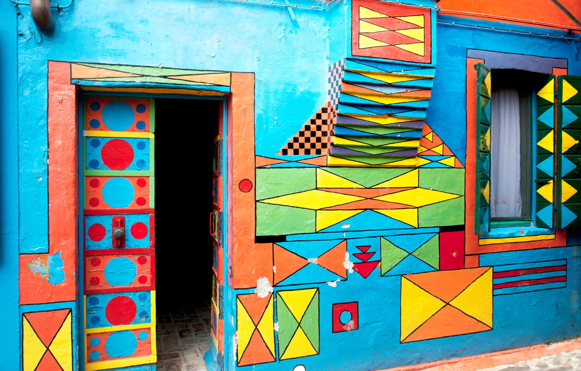 House facade painted with bold geometric patterns in blue, orange, yellow and green around a painted door